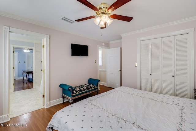 bedroom with wood finished floors, a closet, visible vents, baseboards, and ornamental molding
