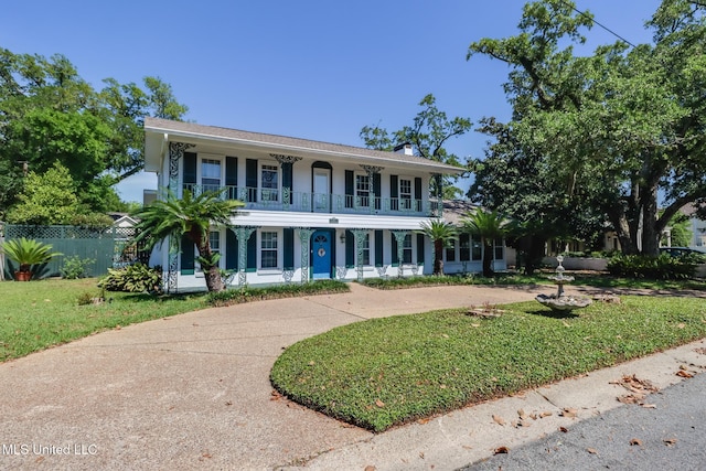 colonial-style house featuring covered porch, a chimney, fence, a front lawn, and a balcony