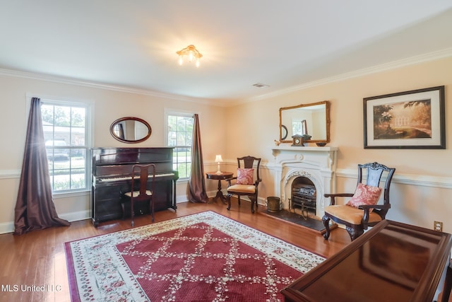sitting room featuring ornamental molding, a wealth of natural light, a fireplace with raised hearth, and wood finished floors