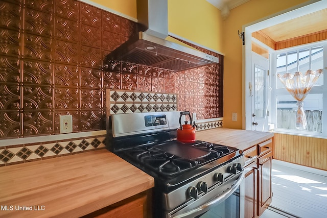 kitchen featuring wood walls, stainless steel gas stove, ventilation hood, ornamental molding, and hardwood / wood-style floors