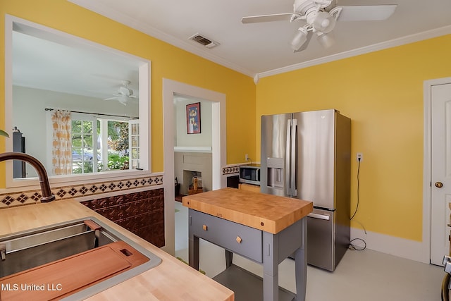 kitchen featuring butcher block countertops, sink, ceiling fan, stainless steel appliances, and ornamental molding