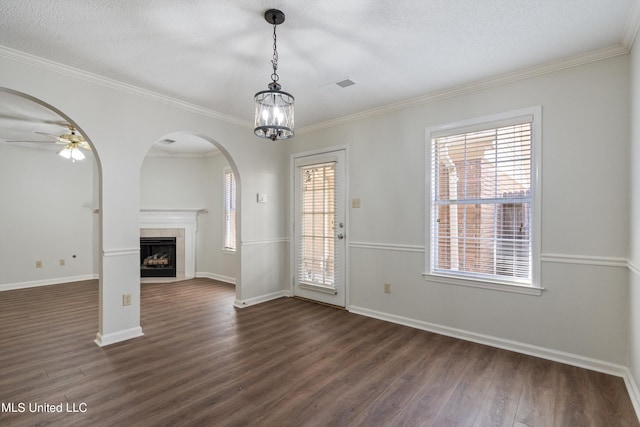 unfurnished living room with dark wood-style floors, crown molding, arched walkways, baseboards, and a fireplace