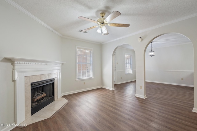 unfurnished living room featuring a tile fireplace, a textured ceiling, arched walkways, wood finished floors, and a ceiling fan