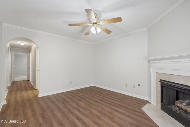 unfurnished living room with wood finished floors, a ceiling fan, arched walkways, ornamental molding, and baseboards