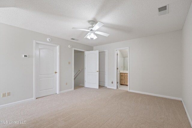 unfurnished bedroom featuring light carpet, a textured ceiling, baseboards, connected bathroom, and ceiling fan
