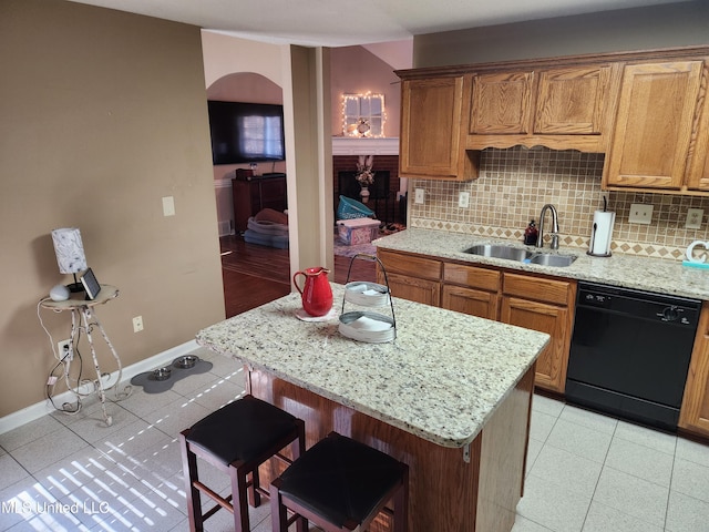 kitchen featuring light stone countertops, black dishwasher, tasteful backsplash, sink, and a breakfast bar area