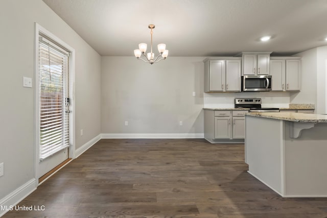 kitchen featuring stainless steel appliances, an inviting chandelier, dark hardwood / wood-style floors, pendant lighting, and a kitchen bar