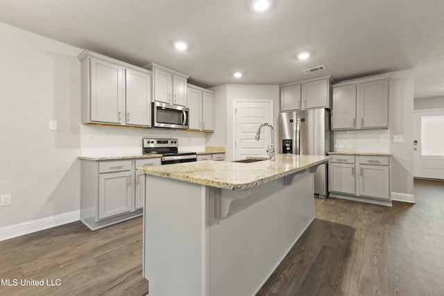 kitchen featuring sink, dark wood-type flooring, gray cabinets, a center island with sink, and appliances with stainless steel finishes