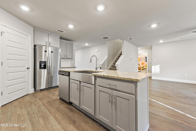 kitchen with appliances with stainless steel finishes, light hardwood / wood-style floors, a kitchen island with sink, sink, and gray cabinets