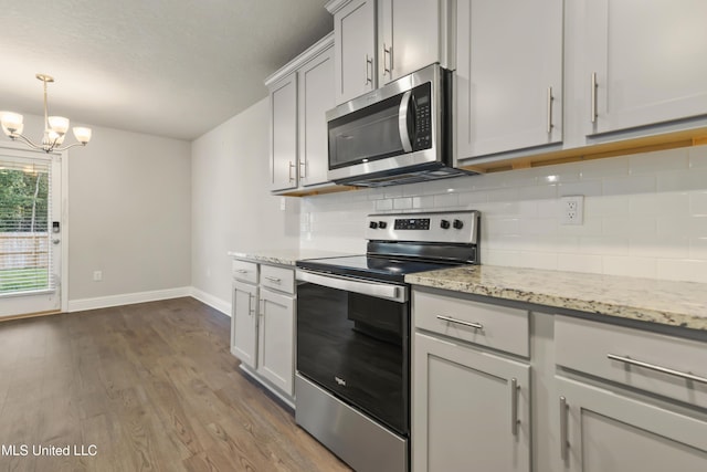 kitchen with decorative backsplash, light stone countertops, a notable chandelier, dark hardwood / wood-style flooring, and stainless steel appliances