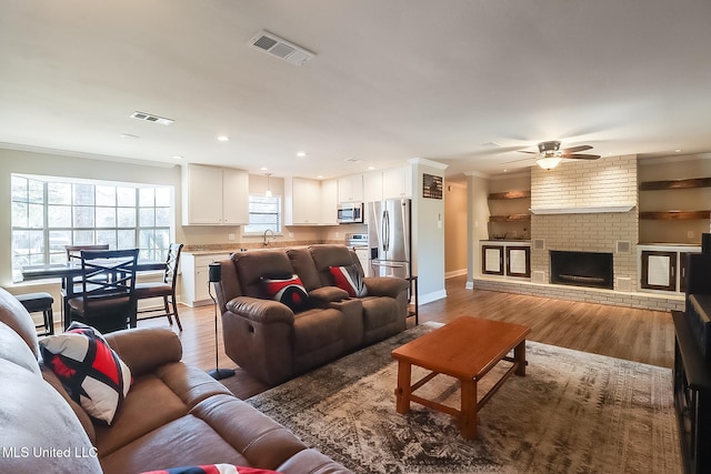 living room featuring ornamental molding, light wood-type flooring, a brick fireplace, and visible vents