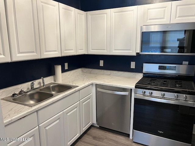 kitchen with a sink, appliances with stainless steel finishes, light countertops, and white cabinetry