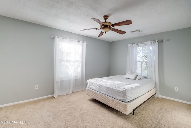 bedroom featuring ceiling fan, light colored carpet, multiple windows, and a textured ceiling