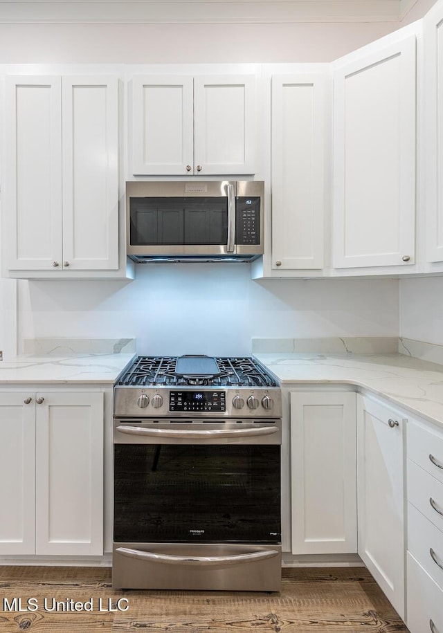433 Main St, Natchez, MS 39120 - kitchen featuring appliances with stainless steel finishes, white cabinets, light stone counters, and light wood-style floors