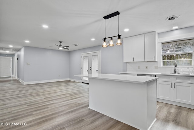 kitchen with pendant lighting, white cabinetry, backsplash, a kitchen island, and french doors