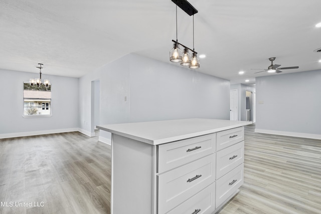 kitchen featuring light hardwood / wood-style flooring, ceiling fan with notable chandelier, white cabinetry, a kitchen island, and decorative light fixtures