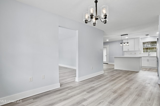 unfurnished living room featuring sink, light hardwood / wood-style floors, and a notable chandelier