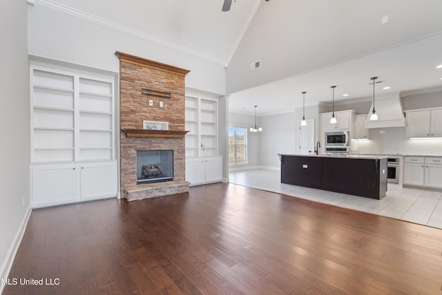 unfurnished living room with ornamental molding, a stone fireplace, baseboards, and light wood-style floors