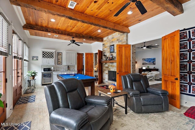 rec room with pool table, light wood-type flooring, a stone fireplace, beamed ceiling, and beverage cooler