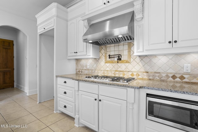 kitchen with white cabinetry, stainless steel appliances, light stone counters, and wall chimney range hood