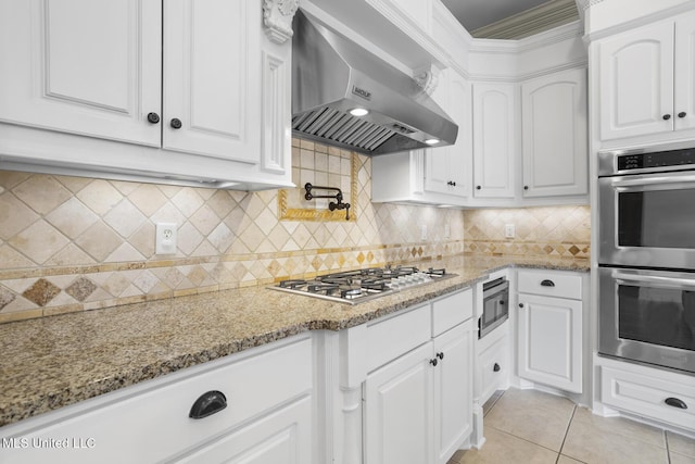 kitchen with white cabinets, light stone countertops, wall chimney exhaust hood, and appliances with stainless steel finishes