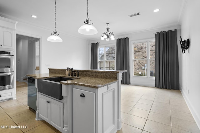 kitchen with double oven, an island with sink, sink, white cabinets, and light tile patterned floors