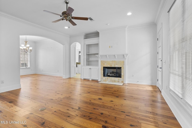 unfurnished living room featuring crown molding, light wood-type flooring, built in features, ceiling fan, and a fireplace