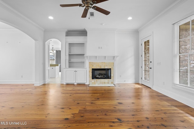 unfurnished living room with built in shelves, plenty of natural light, a fireplace, and hardwood / wood-style flooring