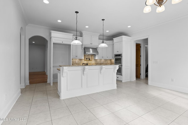 kitchen featuring a kitchen island, white cabinetry, hanging light fixtures, light stone countertops, and wall chimney exhaust hood