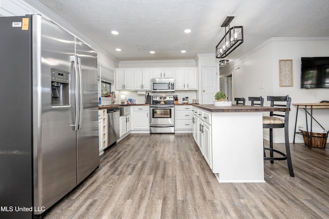 kitchen with wood finished floors, stainless steel appliances, a kitchen breakfast bar, white cabinetry, and ornamental molding