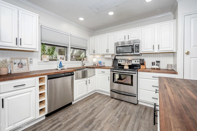 kitchen featuring crown molding, stainless steel appliances, wooden counters, and light wood-style floors