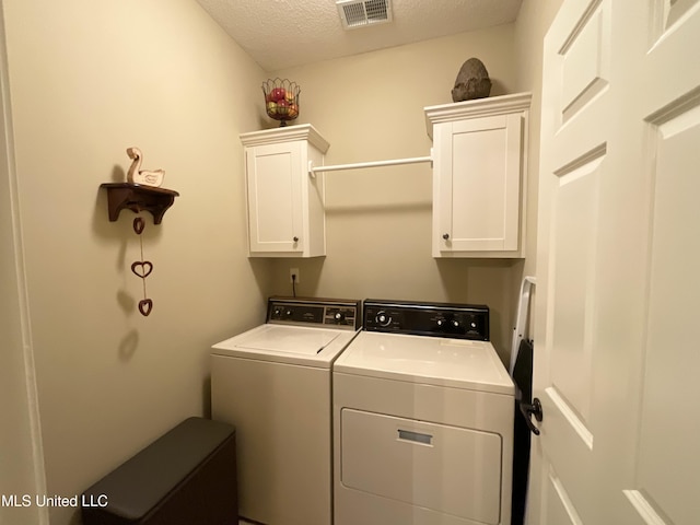 washroom with cabinets, washer and dryer, and a textured ceiling