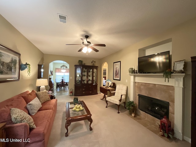 living room with light carpet, a textured ceiling, a tile fireplace, and ceiling fan