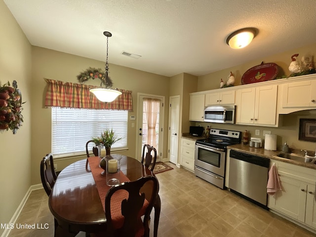 kitchen featuring sink, stainless steel counters, appliances with stainless steel finishes, hanging light fixtures, and white cabinets