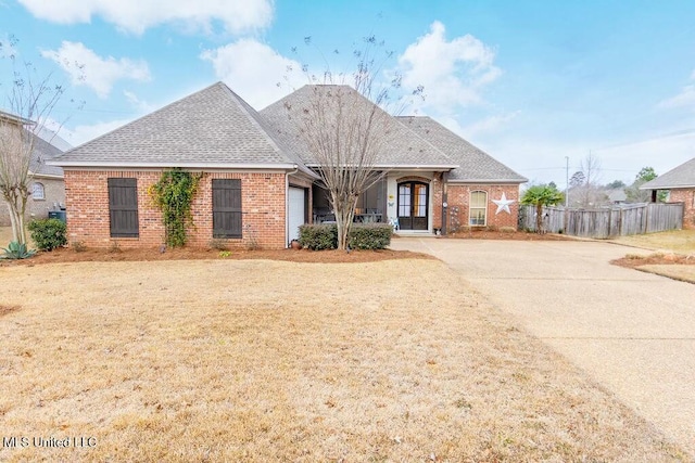 view of front of house featuring driveway, roof with shingles, fence, and brick siding