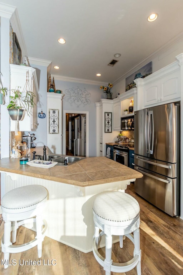 kitchen with stainless steel appliances, visible vents, wood finished floors, a peninsula, and a kitchen bar