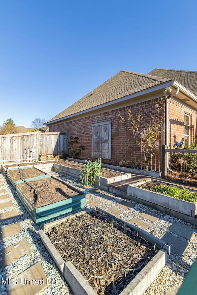 rear view of house with a garden, fence, roof with shingles, and brick siding