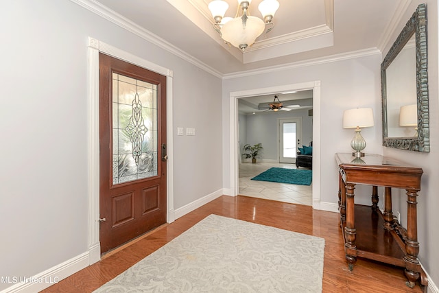 entrance foyer with a raised ceiling, ornamental molding, ceiling fan with notable chandelier, and hardwood / wood-style floors