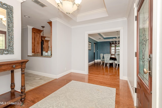 interior space featuring light hardwood / wood-style floors, crown molding, a chandelier, and a raised ceiling