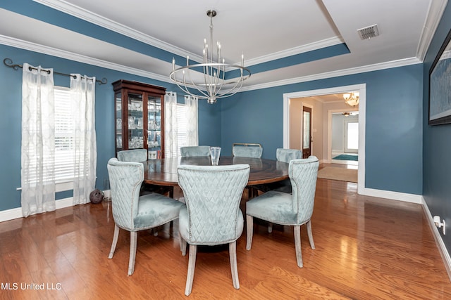 dining space featuring crown molding, a tray ceiling, a notable chandelier, and wood-type flooring