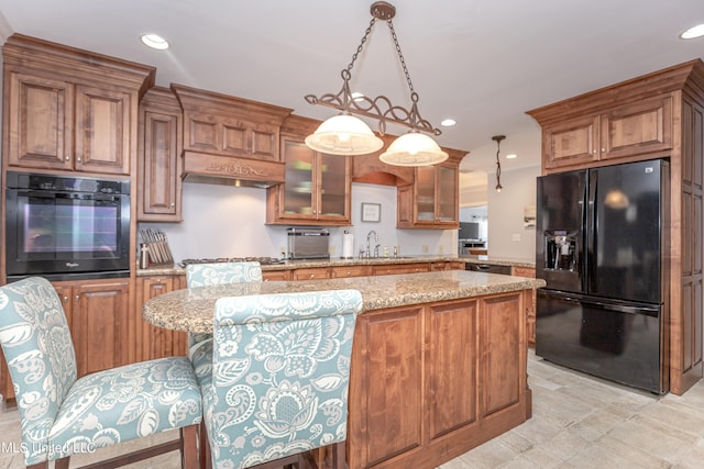 kitchen with black appliances, sink, a center island, hanging light fixtures, and light stone counters