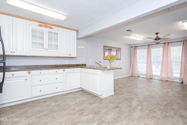 kitchen with sink, kitchen peninsula, ceiling fan, white cabinets, and beam ceiling