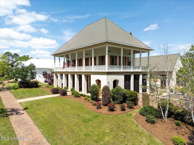 view of front facade with metal roof, ceiling fan, a balcony, and a front lawn