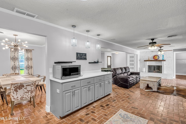 kitchen featuring hanging light fixtures, crown molding, gray cabinets, a textured ceiling, and a fireplace