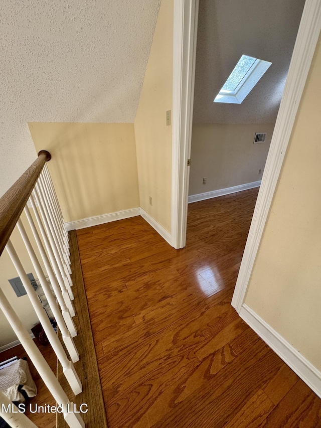 additional living space with a textured ceiling, vaulted ceiling with skylight, wood finished floors, visible vents, and baseboards