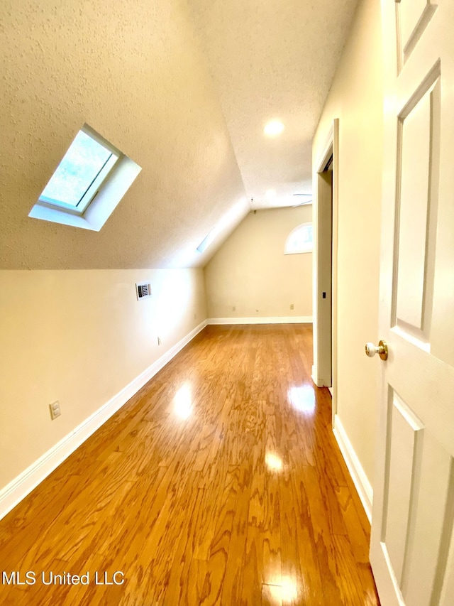 bonus room featuring light wood finished floors, visible vents, baseboards, lofted ceiling with skylight, and a textured ceiling