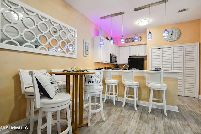 kitchen featuring light hardwood / wood-style flooring, white cabinets, hanging light fixtures, and a breakfast bar