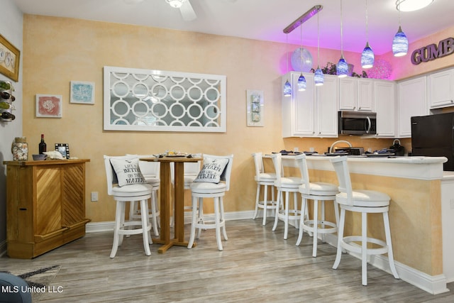 kitchen with a kitchen bar, white cabinetry, hanging light fixtures, and light wood-type flooring