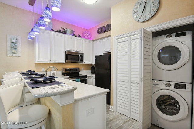 kitchen with kitchen peninsula, stainless steel appliances, decorative light fixtures, white cabinetry, and stacked washer / dryer