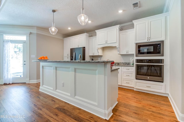 kitchen with appliances with stainless steel finishes, white cabinetry, a textured ceiling, a center island with sink, and decorative light fixtures